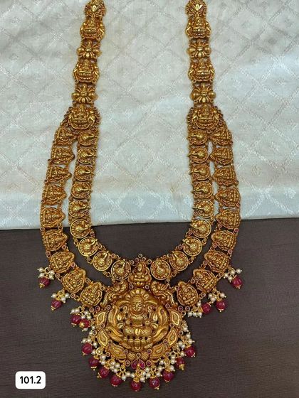 This grand double-layered temple haram is a true statement piece. Made from 92.5 silver with gold plating, it features intricate goddess motifs and is finished with ruby-colored beads and pearls.