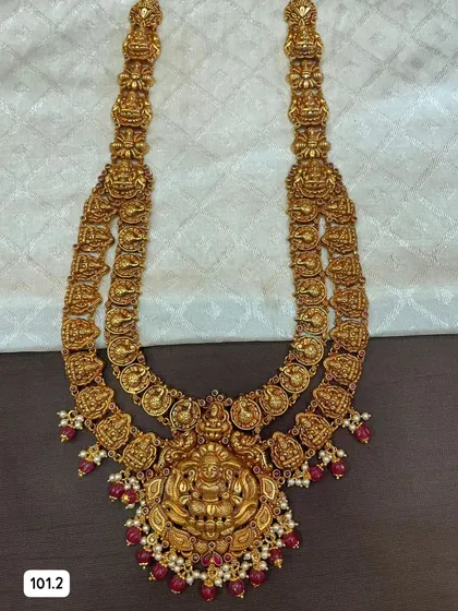 This grand double-layered temple haram is a true statement piece. Made from 92.5 silver with gold plating, it features intricate goddess motifs and is finished with ruby-colored beads and pearls.