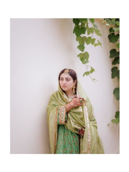 A simple yet elegant full-length portrait of the bride in her beautiful green outfit, set against a clean, white wall.
