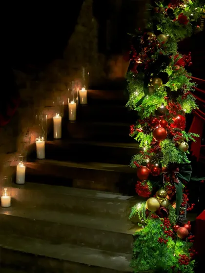 A staircase at Gigi restaurant, decorated for Christmas with a lush garland of greenery, red ornaments, and glowing candles.