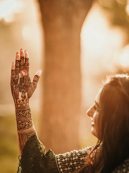 A beautiful, artistic shot of a client admiring her mehndi. The golden hour light makes the henna glow.