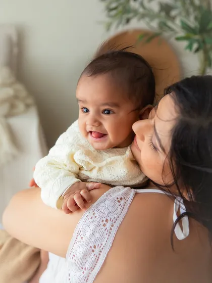 A happy 6-month-old baby snuggled safely on her mother's shoulder. This portrait is full of warmth, comfort, and the sweet connection between them.