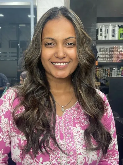 A happy client showing off her new wavy hairstyle with subtle, natural-looking highlights that add just the right amount of brightness.