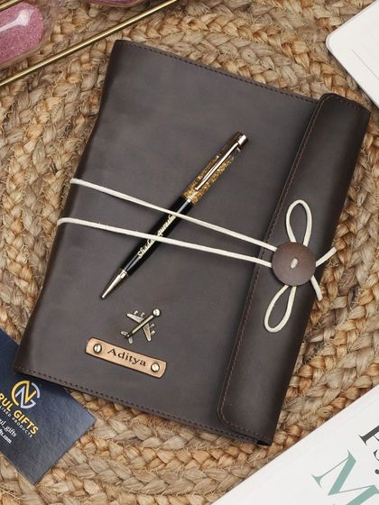 A brown leather thread-bound diary and pen set with an airplane charm.