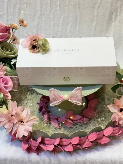 A beautiful gift platter for an engagement or Roka. A luxury watch box is presented on a tray adorned with a delicate arrangement of pink and green artificial flowers.