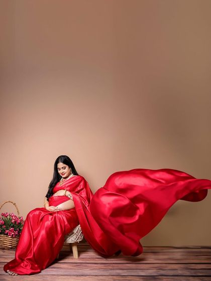 A dynamic shot of the mother-to-be in a flowing red satin saree. The movement of the fabric adds a touch of drama and artistry to the portrait.