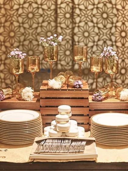 An elegant and symmetrical buffet station setup, featuring gold-rimmed plates, gold cutlery holders, and beautiful floral arrangements.