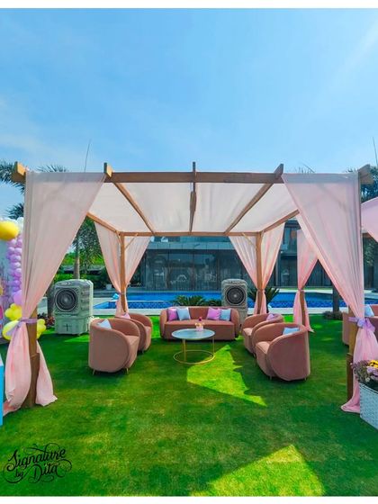 A comfortable and chic lounge area for parents, set up under a shaded canopy by the pool. The blush pink furniture complements the party's pastel colour scheme.