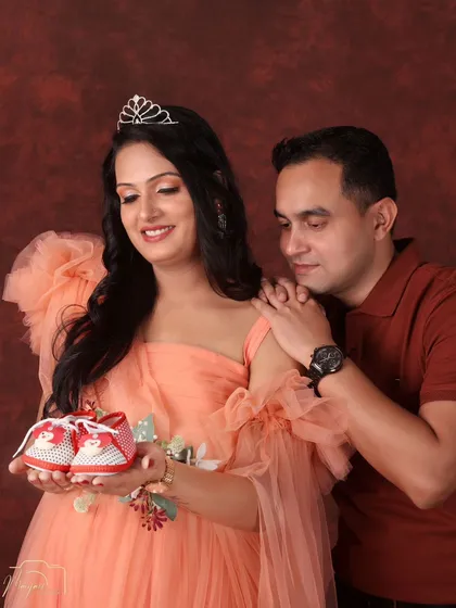 A fairytale in peach tones. The mom-to-be, wearing a delicate tiara, holds up tiny baby shoes as her partner looks on with love, creating a sweet and hopeful portrait.