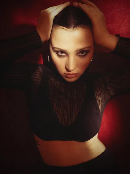 An intense, direct portrait from the same series. The model's hands framing her face and her confrontational gaze create a powerful and captivating image.