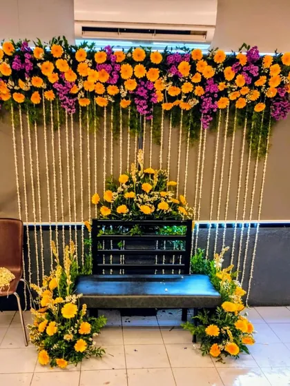 A bright and cheerful seating arrangement for the bride's Haldi. The backdrop is decorated with yellow and purple gerbera daisies and hanging jasmine, perfectly framing the seating area for the ceremony.