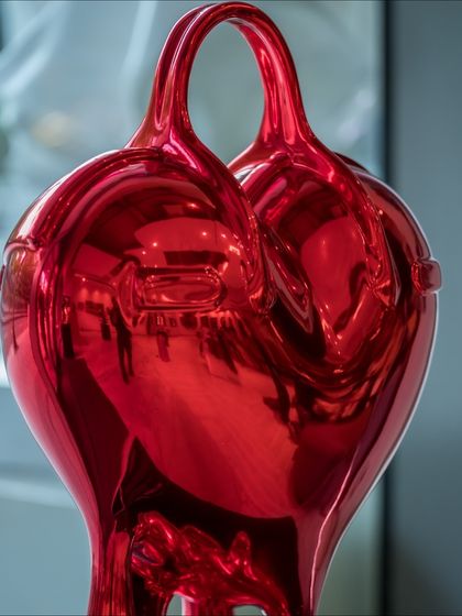 A close-up of the "Melting Affection" sculpture, where the red chrome surface reflects the gallery around it.