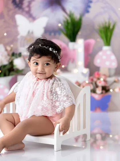 A sweet princess sitting on a tiny bed in her butterfly-themed first birthday setup.