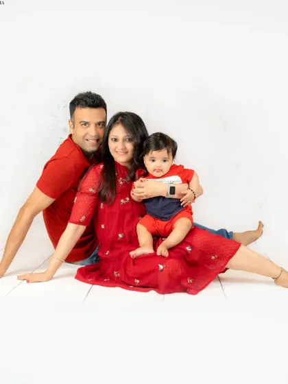 A relaxed, floor-seated family portrait. The family's coordinated red outfits and comfortable poses create a warm and inviting atmosphere.