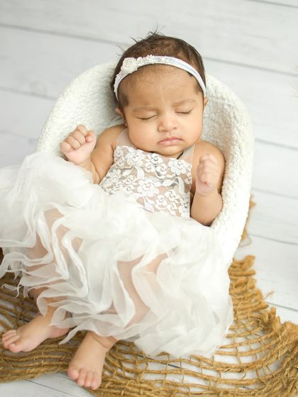 A close-up of the baby in the white lace dress, showing her little fists clenched in sleep.