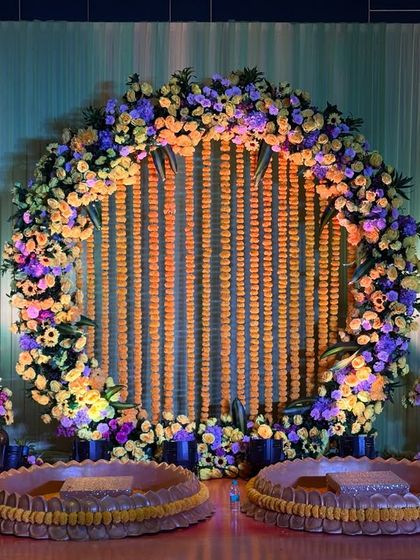 The full view of the circular marigold backdrop, complete with traditional brass pots for the Haldi ceremony. The lighting enhances the rich colors of the decor.
