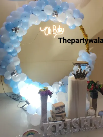 A simple and elegant baby shower ring decoration with blue and white balloons. The "Oh Baby" neon sign and a single pedestal for the cake make it a chic and modern choice.