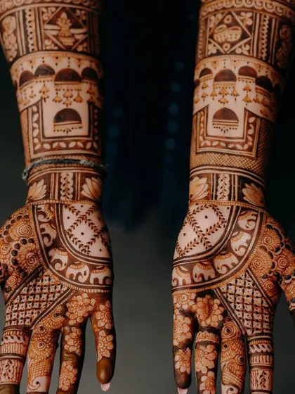 A dark, moody shot of the bridal mehendi, highlighting the intricate patterns and the beautiful contrast against the dark background.