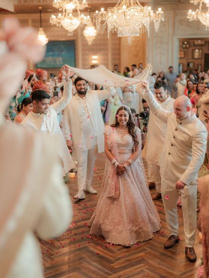 The bride makes her way to the mandap, escorted by her brothers under a traditional phoolon ki chadar, a classic and emotional wedding moment.