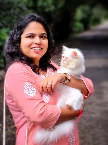 A lovely individual portrait taken outdoors. The woman's warm smile as she holds her beautiful Persian cat creates a heartwarming and personal photo.