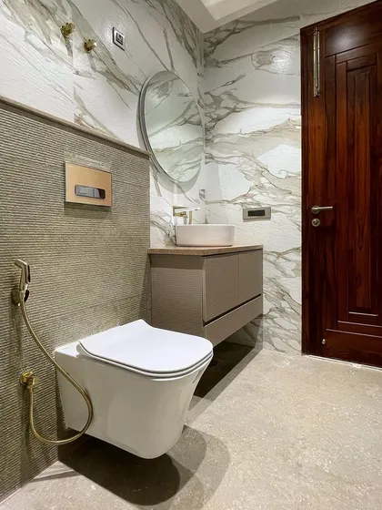 This elegant bathroom combines large-format marble-look tiles with a textured stone accent wall behind the toilet. The brushed gold sanitary fixtures add a touch of warmth and luxury.