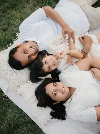 An overhead shot of a family lying on a blanket, looking up at the camera with bright smiles. This is a fun and unique angle for an outdoor family photoshoot.