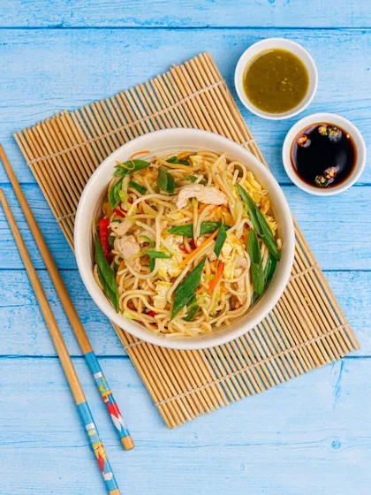 A top-down shot of Hakka noodles, styled cleanly on a bamboo mat for an Asian cloud kitchen menu.