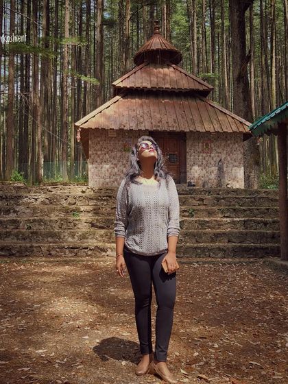 Looking up at a forest temple in Uttarakhand. A simple grey sweater and black leggings are a practical choice for exploring spiritual sites in the mountains.
