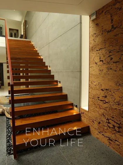 The floating wooden staircase in the "Waterfront Home" is a sculptural element in itself. It rises alongside a textured cork wall and overlooks the indoor water feature, blending natural materials and modern design.