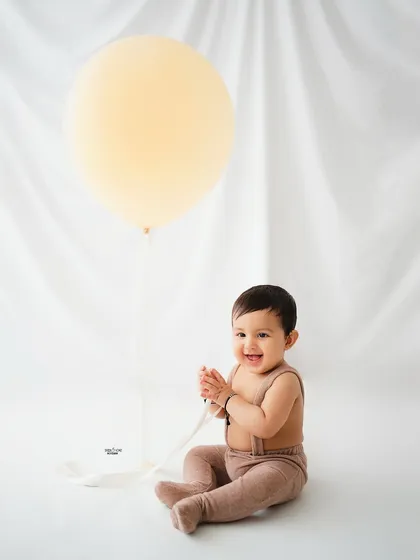 A happy baby boy clapping his hands, with a simple giant balloon as a prop.