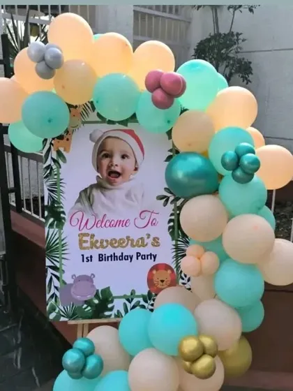A welcome sign for a first birthday party, framed with a pastel-colored balloon garland.