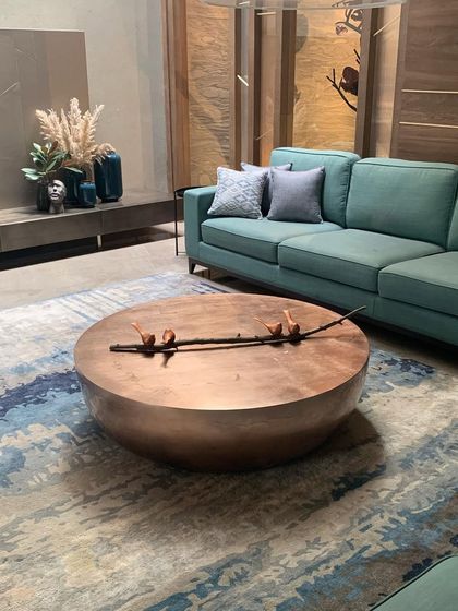 A wide shot showing the hammered copper coffee table in its living room setting, complementing the blue tones of the sofa and rug.