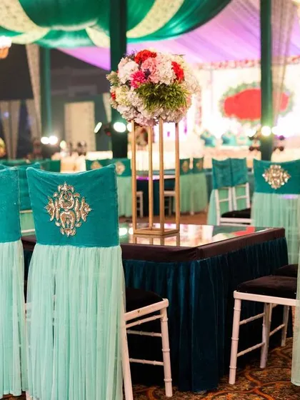 For a grand indoor reception, we designed these custom chair covers in a striking teal color. The elegant draping and gold embroidered detail on the chairs add a touch of luxury to the guest dining tables.