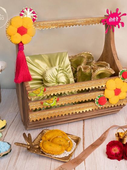 A unique wooden crate hamper for Holi, decorated with felt flowers and filled with fabric-wrapped gifts. It's a rustic yet chic way to share festive joy.