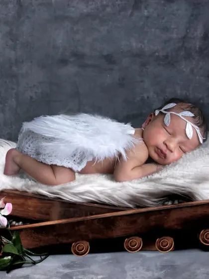 A baby boy with angel wings sleeping on a rustic prop against a textured grey background.
