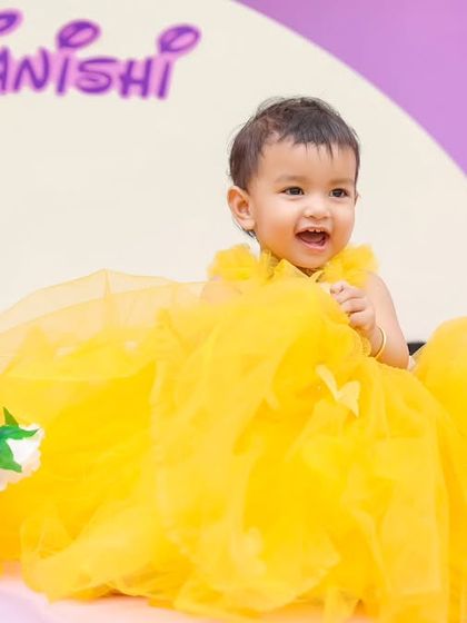 A radiant smile from the birthday girl in her bright yellow dress. This candid shot captures the pure happiness of a child enjoying her special day, set against a simple yet elegant Disney-themed backdrop.