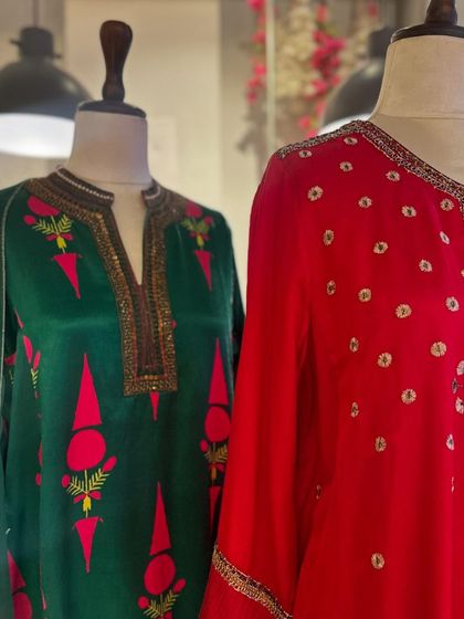 A detailed view of the contrast between a deep green kurta with pink accents and a bright red embroidered piece.