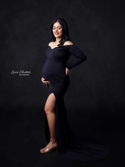 The elegance of a simple black gown, highlighting the beautiful silhouette of pregnancy against a dark studio background.