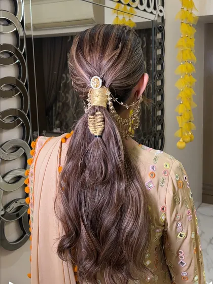 A textured ponytail with a unique, woven hair accessory. This style combines the ease of a ponytail with the elegance of detailed craftsmanship, perfect for a festive look.