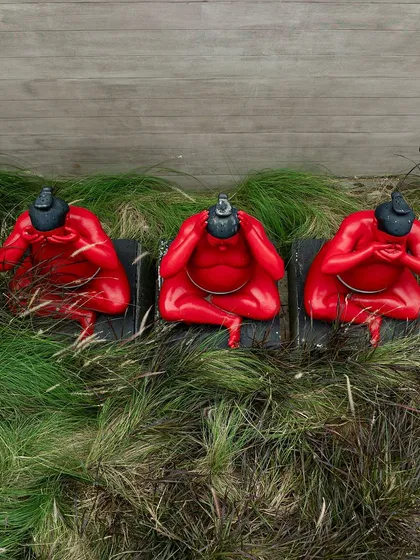 An aerial view of the three red sumo wrestler sculptures nestled in tall grass. This perspective highlights their vibrant color and playful forms within the green landscape.