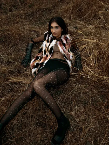 An overhead shot from a fashion story set in a dry, grassy field. The model's pose and the textures of the faux fur and sparkling tights contrast with the rustic, natural setting.