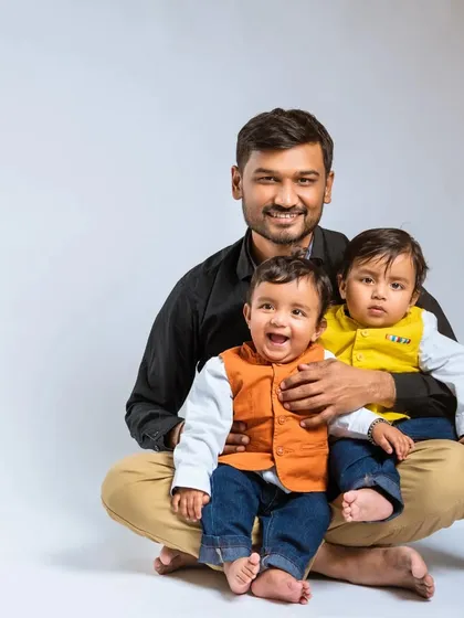 A proud father with his twin baby boys. The boys' colorful vests add a playful touch to this studio portrait, highlighting the joy and energy of life with twins.