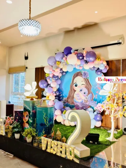 A wide view of a mermaid-themed party, showing the full stage setup in a home. This design includes multiple character props and light-up numbers for a joint birthday celebration.