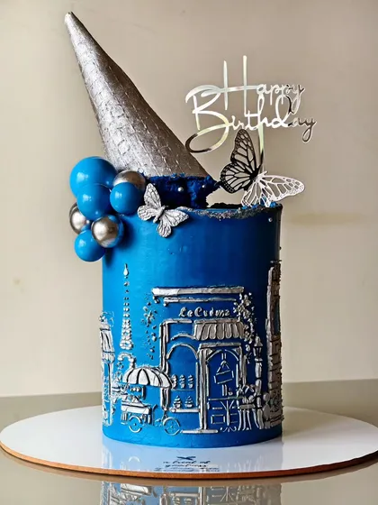 I brought a touch of Paris to this birthday with a detailed bas-relief cityscape, sculpted entirely from buttercream. The silver finish on the classic blue cake, topped with a modern cone and delicate butterflies, creates a truly unique and elegant centerpiece.