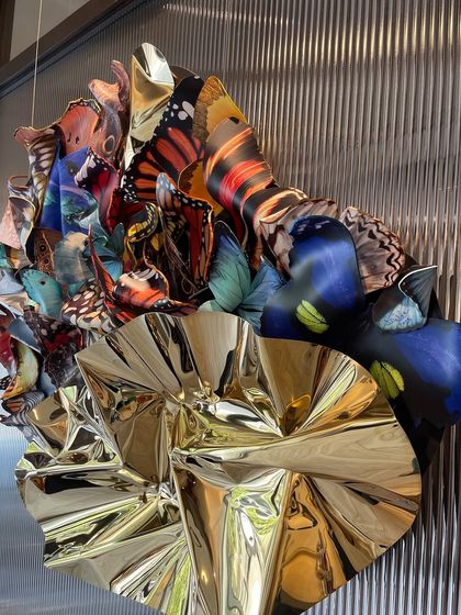 "Emphemeral Reflections," a wall installation where a cluster of colorful butterflies meets a sheet of crumpled golden metal.