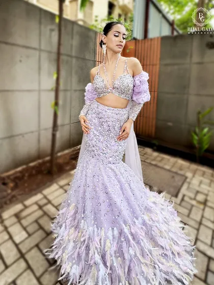 A breathtaking western-inspired bridal look in a lilac gown with feather details. The makeup is kept sleek and modern, with a wet-look hairstyle and soft purple tones on the eyes.