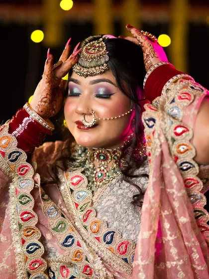 The bride adjusts her maang tikka, a candid-style shot that showcases the wearability and beauty of the makeup.