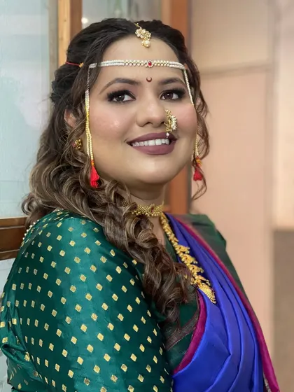 A modern Maharashtrian bridal look. The soft, curly open hairstyle is a contemporary choice that pairs beautifully with the traditional saree and mundavalya.