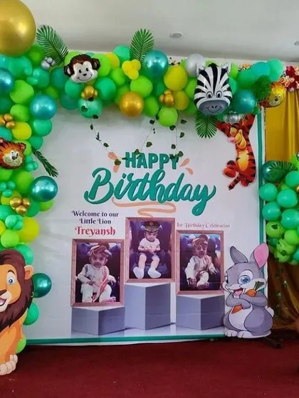 A vibrant jungle birthday backdrop with a balloon arch, large lion and rabbit cutouts, and a personalized banner with the birthday boy's photos.