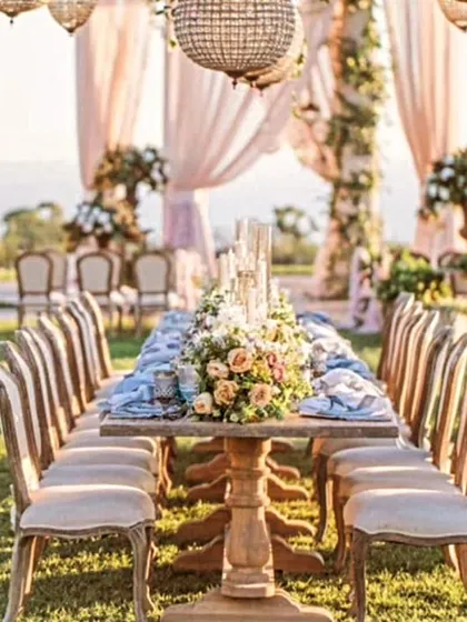 An elegant outdoor dining setup for an intimate wedding or event, featuring a rustic wooden table, beautiful floral centerpieces, and hanging chandeliers.